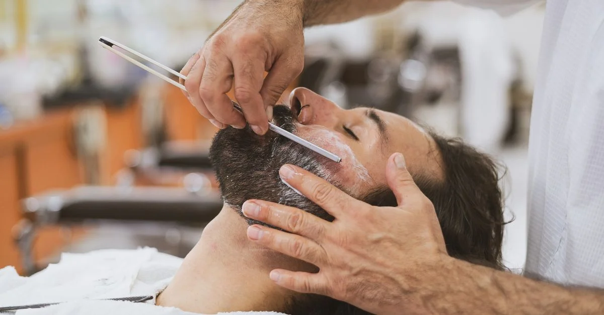 Coiffeur effectuant un rasage classique avec un rasoir droit. Toilettage du visage dans un salon de coiffure.