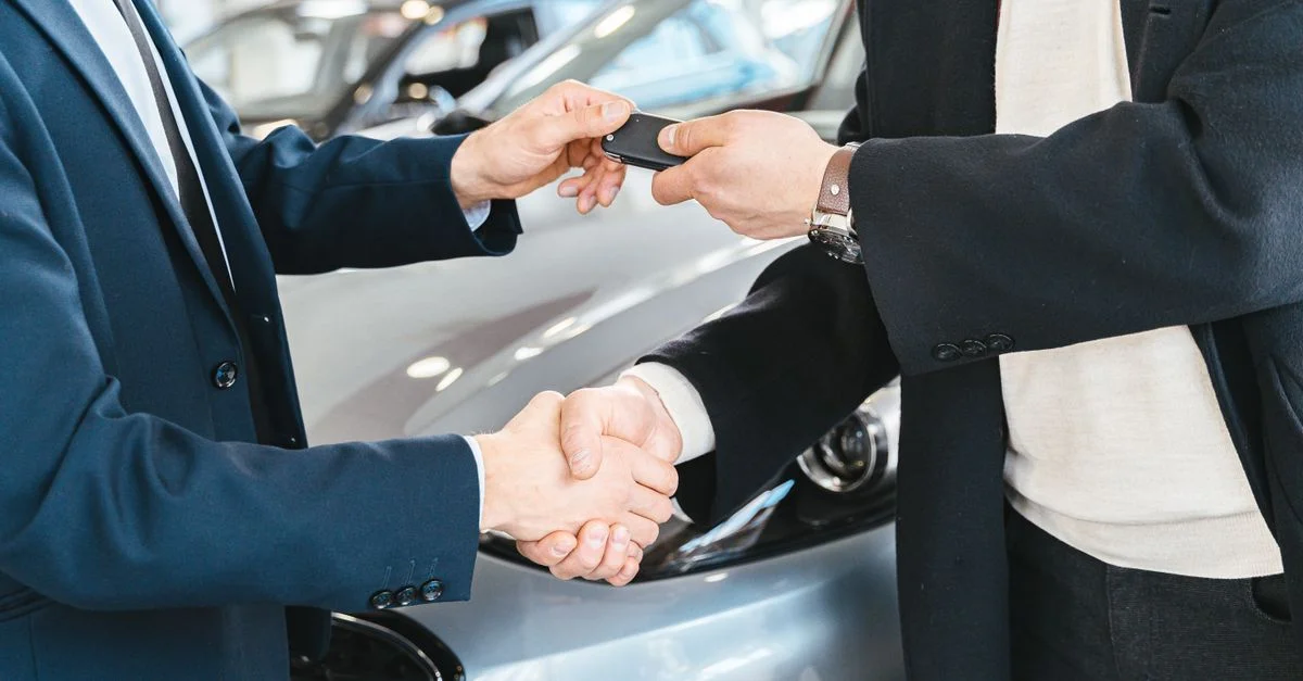 Deux hommes d'affaires se serrant la main et échangeant des clés de voiture dans une concession automobile. Symbolise un accord réussi.
