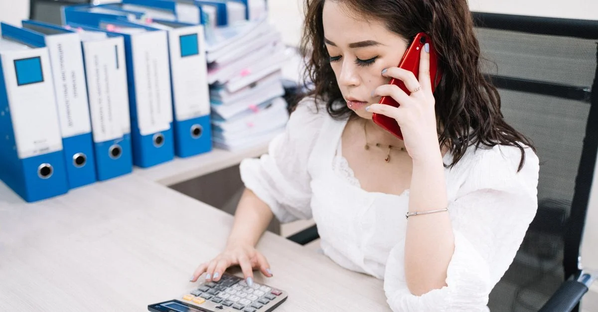 Femme d'affaires multitâche avec calculatrice et téléphone portable à son bureau.