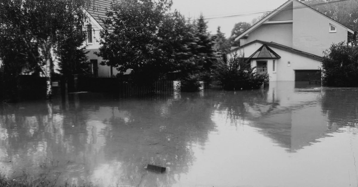 Photo en noir et blanc d'une rue suburbaines inondée, maisons immergées dans l'eau.
