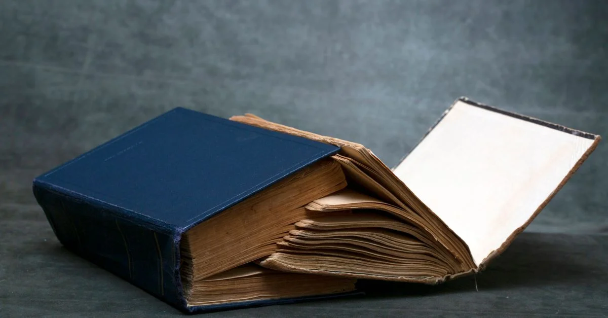 Un vieux livre usé à couverture rigide bleue, ouvert sur une surface sombre, laissant apparaître des pages jaunies.
