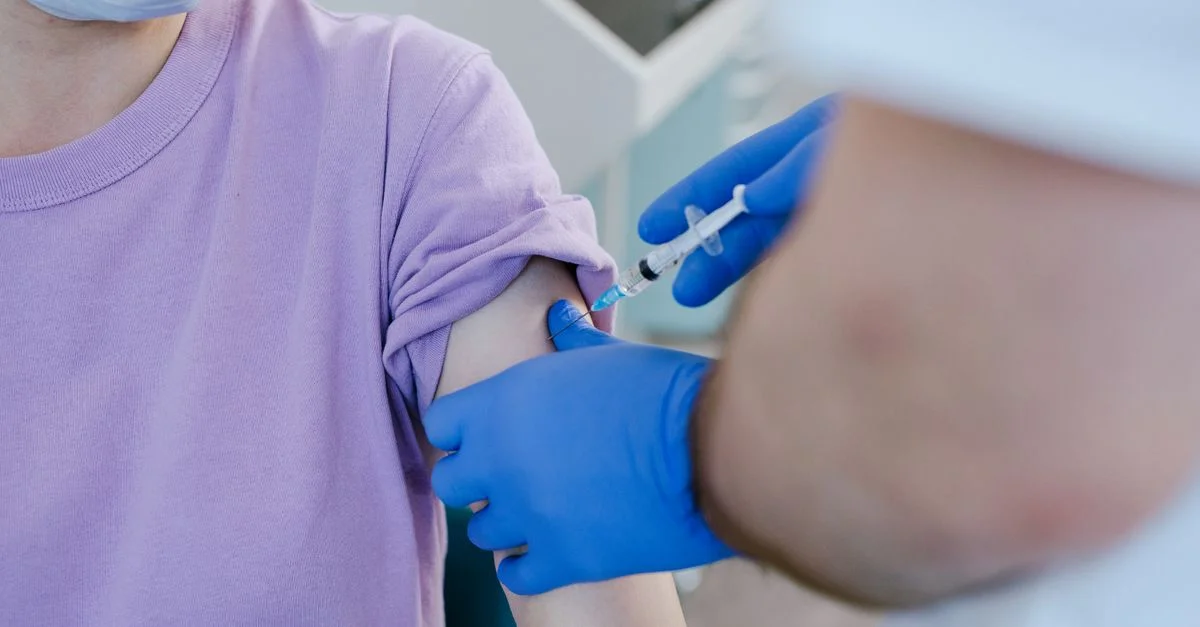 Gros plan d'un professionnel de santé administrant une injection de vaccin à un patient portant une chemise violette.