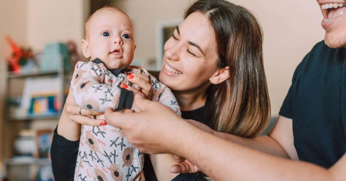 Un moment familial joyeux avec des parents tenant leur bébé à l'intérieur, mettant en avant l'amour et la complicité.