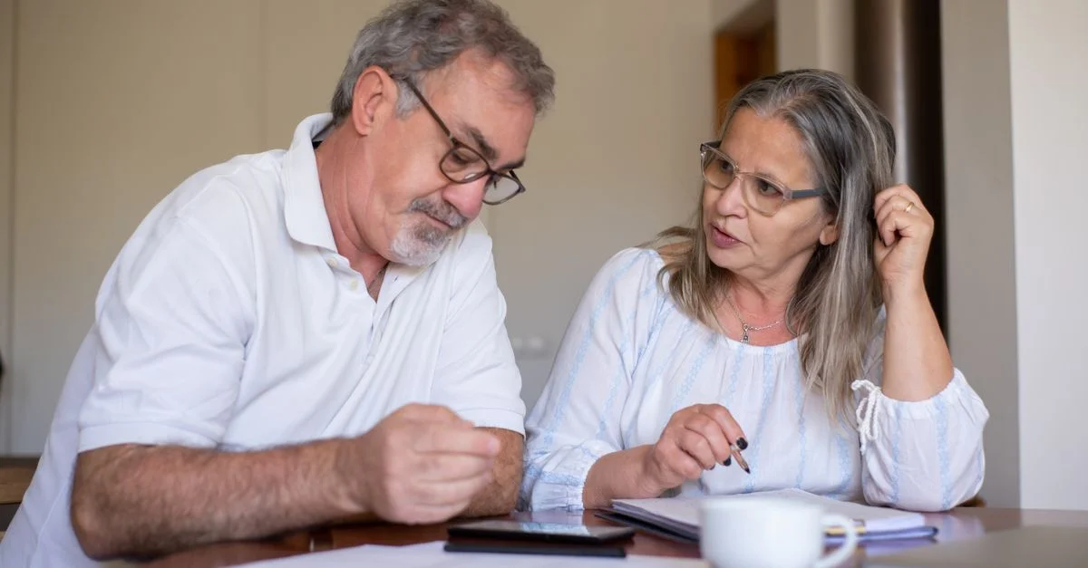 Couple de seniors examinant des documents et gérant leurs finances ensemble à la maison, montrant collaboration et attention.