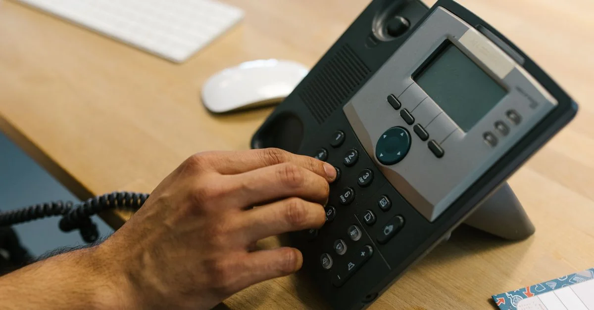 Une main composant un téléphone sur un bureau en bois. Environnement de bureau avec un clavier et un planificateur.