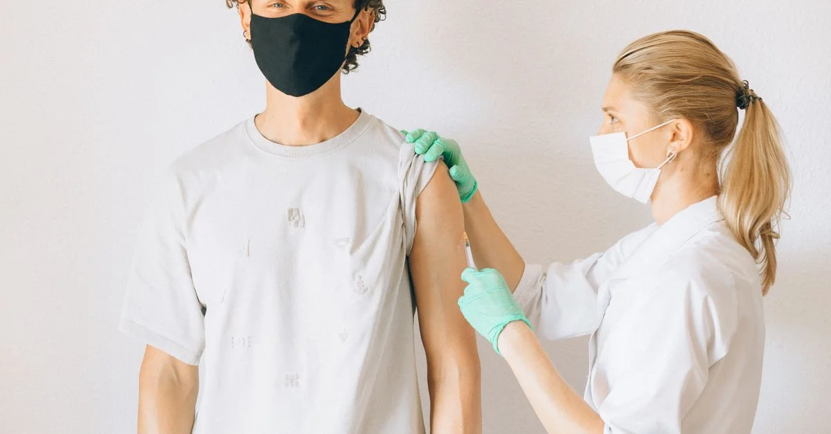Un professionnel de santé administrant une injection de vaccin à un homme masqué dans une clinique.