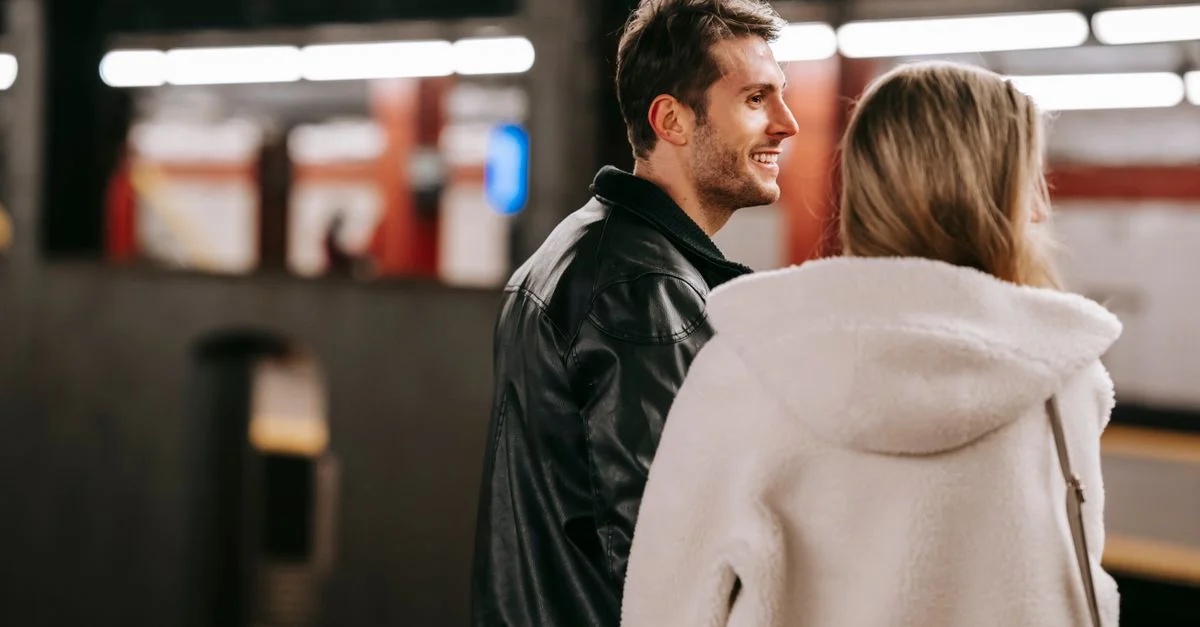Un couple heureux souriant sur le quai d'une station de métro, portant des vêtements chauds, éclairé par un éclairage intérieur.